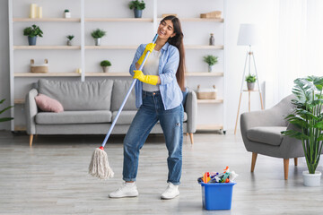 Portrait of excited woman cleaning floor singing holding mop