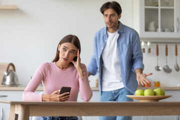 Unhappy angry upset offended young husband yelling at wife with smartphone, woman ignoring guy on...