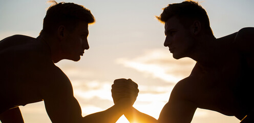 Silhouette of hands that compete in strength. Rivalry, closeup of male arm wrestling. Men measuring forces, arms. Two men arm wrestling. Rivalry, vs, challenge, hand wrestling. Sunset, sunrise