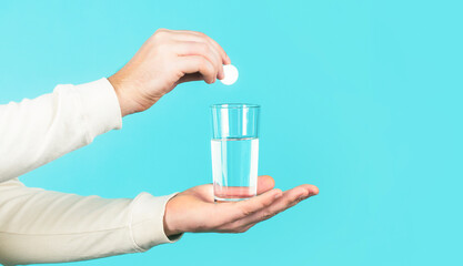White pill and a glass of water in man hands. Health concept. Close up of man holding a pill. Glass of water tablet. Glass with efervescent tablet in water with bubbles