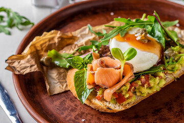 Fototapeta na wymiar Bruschetta with avocado, salted salmon, microgreens and poached egg