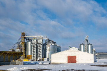 Obraz premium agro silos granary elevator in winter day in snowy field. Silos on agro-processing manufacturing plant for processing drying cleaning and storage of agricultural products, flour, cereals and grain.