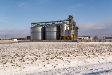 Obraz premium agro silos granary elevator in winter day in snowy field. Silos on agro-processing manufacturing plant for processing drying cleaning and storage of agricultural products, flour, cereals and grain.