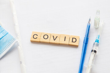 The inscription covid on a medical background, next to the vaccine, syringe, pen, protective mask....