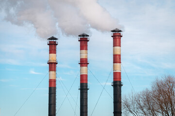 Three factory chimneys emit puffs of smoke against the blue sky. The concept of air pollution, environment, industry and ecology, global warming.