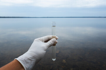  The scientist is taking water sample of sea water. Test tube with water in a hand. Sea water pollution concept. Cloudy sky..... - obrazy, fototapety, plakaty