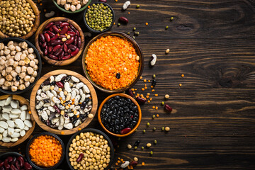 Legumes, lentils, chikpea and beans assortment in different bowls on wooden table. Top view. Vegan food, alt meat.