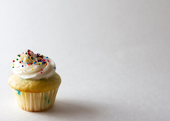 Close up view of a mini cupcake decorated with spring colored mini ball candy sprinkles.  White background with copy space.