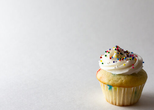 Close up view of a mini cupcake decorated with spring colored mini ball candy sprinkles.  White background with copy space.