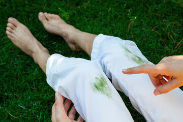 Hand showing dirty stain of grass on white pants from unexpected accident. top view. daily life stain concept. outodoors.  - obrazy, fototapety, plakaty