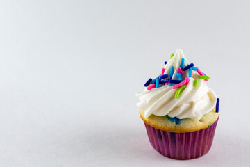 Close up view of a mini cupcake decorated with spring colored candy sprinkles.  White background with copy space.