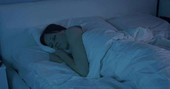 Young woman going to sleep under duvet blanket in a cosy bed in a bedroom. Concept of comfort