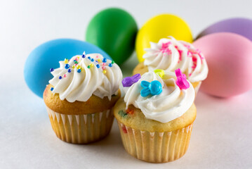 Assorted mini cupcakes with Easter eggs blurred in the background.  White background.