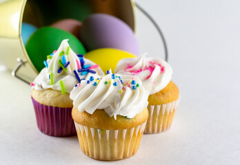 Assorted mini cupcakes with gold pail and Easter eggs blurred in the background.  White background.