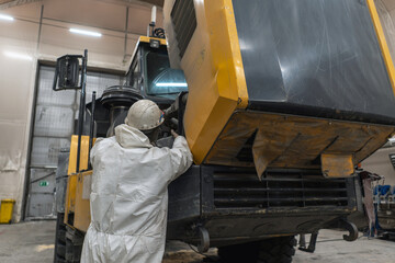 A mechanic in a helmet repairs an articulated dump truck in an industrial garage.