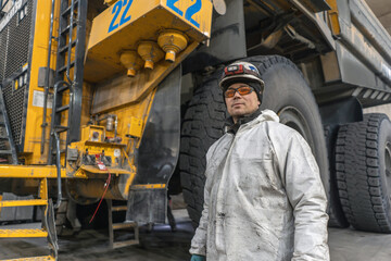A mechanic in a helmet and goggles stands in front of a dump truck in the garage.  © CjVitoS