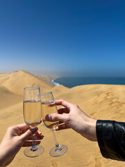 Young couple clink glasses with champagne. Sandwich Harbour in Namibia at coast.