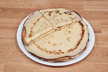 A lot of homemade thin round pancakes on white plate. Top view. Traditional russian sweet dessert. Delicious pancakes on wooden table.