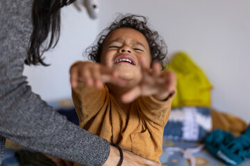 Latin American boy (2) is upset because his mother is changing his clothes. Concept of childhood...