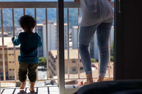 Latin American Mom (30) And Her Son (2), Standing On The Balcony Look Out Over The City From The Top Of Their Apartment. Mother's Day Concept, Single Mother.