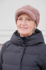 Close-up winter portrait of smiling senior woman looking at camera, wearing faux pink fur cap.