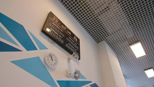 Digital scoreboard clock and loudspeakers on wall with blue pattern in hallway of contemporary sports stadium low angle shot