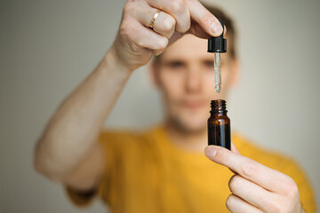 Vitamins and supplements. Hand holding pipette of Hemp oil. Close up man uses CBD oil. Medical...