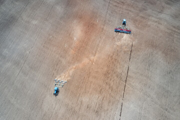 Spring sowing. Two tractors are working on a plowed field: one with a seeder, the other rolls the sown grain. Shooting from a drone.