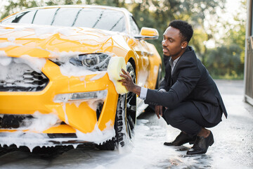 Car washing outdoors ar self wash service station. Handsome African Confident male entrepreneur in...