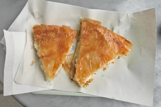 Two slices of fresh juicy burek - traditional pie with cheese, unwrapped, standing on the plate, on a table