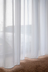 Light and see through concept, Classic white sheer curtains hanging by the window and brown carpet in the room with warm sunlight, Blurred outside view as background.