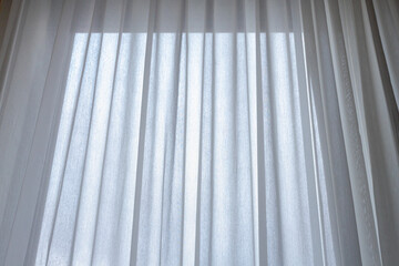 Light and see through concept, Classic white sheer curtains hanging by the window and brown carpet in the room with sunlight, Blurred outside view as background.