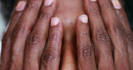 Fototapeta premium Pensive African man covering face with hands, black person revealing eyes portrait thinking