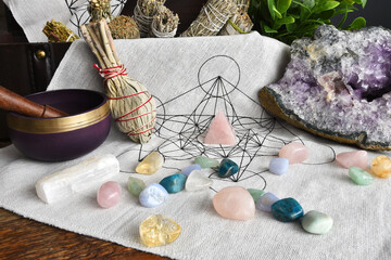 A low angle image of a sacred geometry grid cloth with sage smudge sticks, healing crystals and...
