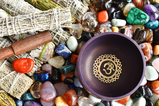 A top view image of a purple meditations singing bowl with white sage smudge sticks and healing crystals.