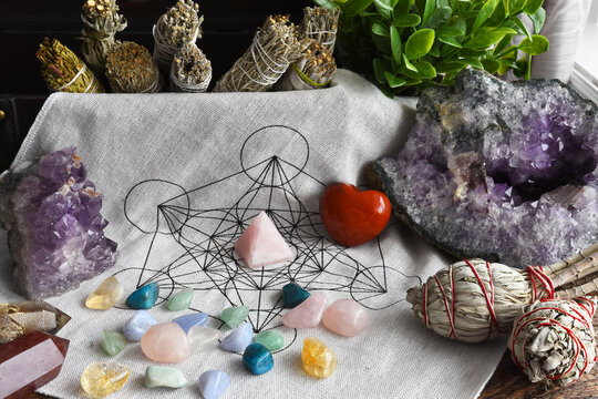 A low angle image of a sacred geometry grid cloth with sage smudge sticks and healing crystals. 