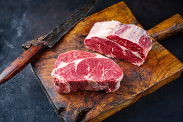 Raw dry aged Angus rib-eye beef steaks offered as close-up on an old rustic wooden board
