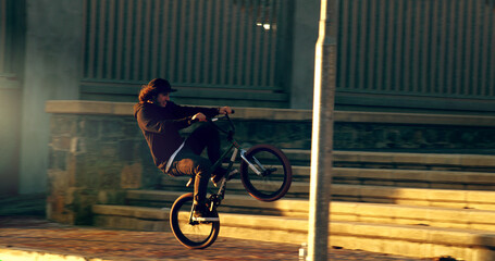 Popping a wheelie. Full length shot of a young male BMX rider doing tricks around the city.