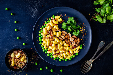 Gnocchi with green peas, bacon and mushrooms on black wooden table
