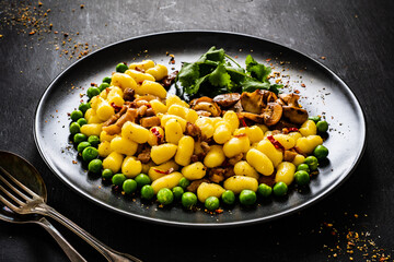 Gnocchi with green peas, bacon and mushrooms on black wooden table
