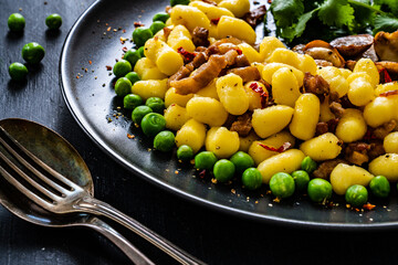 Gnocchi with green peas, bacon and mushrooms on black wooden table
