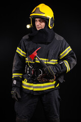 Fototapeta premium Firefighter fully equipped with helmet and ax in smoke, black background