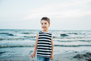 portrait of a attractive handsome smiling boy in a vest. Funny cute child in summer by stormy sea weather. Happy childhood.