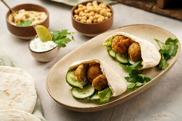 Traditional oriental chickpea deep fried falafel in flatbread pita, tzatziki yoghurt sauce, hummus, fresh lime and green cilantro on light surface