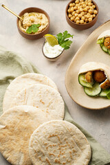 Traditional oriental chickpea deep fried falafel in flatbread pita, tzatziki yoghurt sauce, hummus, fresh lime and green cilantro on light surface