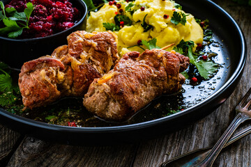 Wrapped pork with potato puree and red beets on wooden table
