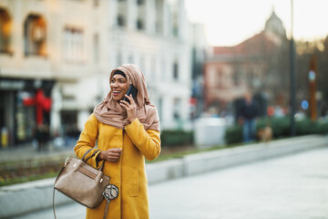 Fototapeta premium Black Muslim Woman With Hijab Using Smart Phone On The Street