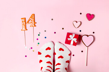 Feet in white socks with red hearts and sweet gifts on a pink background. Delicious gingerbread in the shape of a heart for Valentine's Day. Celebration on February 14 with desserts and sweets