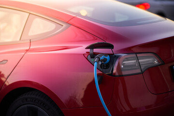 Modern red electric vehicle at the time of charging connected to charging station.