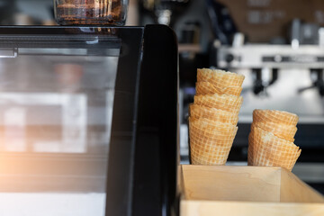 Many empty baked waffle cones and paper cups for ice cream stacked at display counter window of street food takeaway cafe window. Sweet desserts and hot tea coffee cafeteria